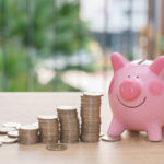 Pink piggy bank with stack coins on wooden desk – save money con