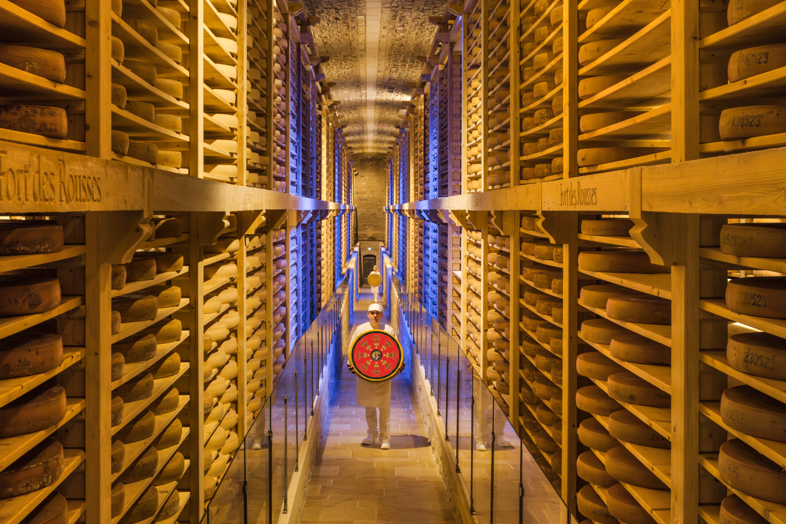 Cave à fromage avec un artisan fromager au milieu avec une meule de comté