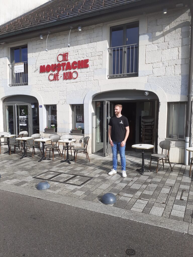 Café Chez Moustache avec le propriétaire devant sur la terrasse