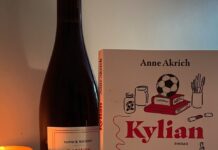 Une bouteille de vin, un livre intitulé Kylian par Anne Akrich, une bougie allumée et un carnet avec un stylo.