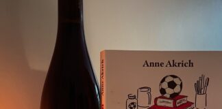 Une bouteille de vin, un livre intitulé Kylian par Anne Akrich, une bougie allumée et un carnet avec un stylo.