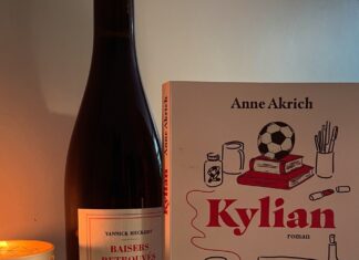 Une bouteille de vin, un livre intitulé Kylian par Anne Akrich, une bougie allumée et un carnet avec un stylo.