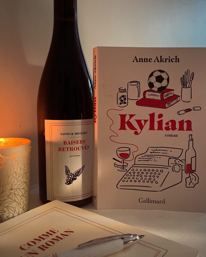 Une bouteille de vin, un livre intitulé Kylian par Anne Akrich, une bougie allumée et un carnet avec un stylo.