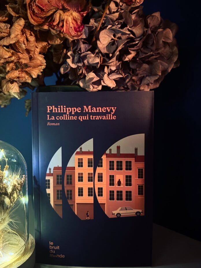Couverture du roman La colline qui travaille de Philippe Manevy, montrant une illustration urbaine avec immeubles, voiture et cloche décorative à fleurs séchées.