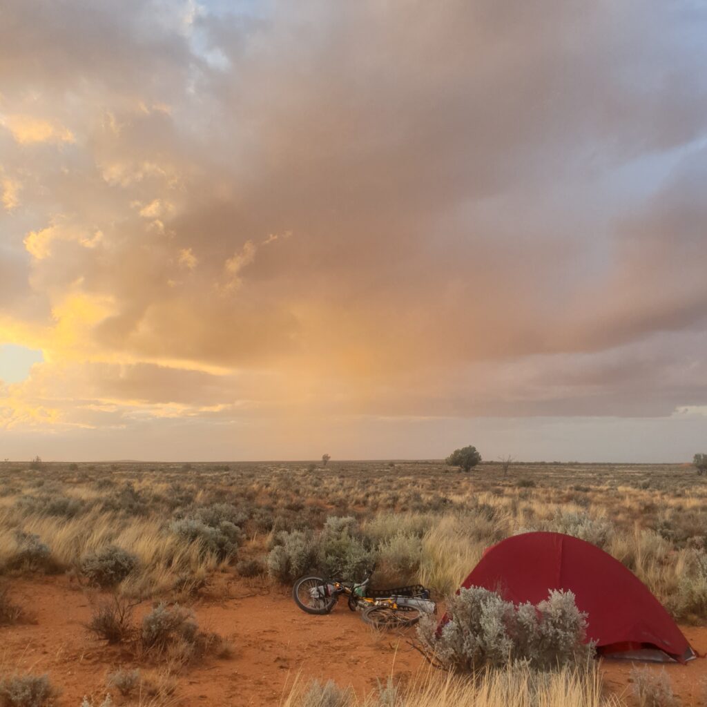 Bivouac paisible en Australie centrale avec tente et vélo sous ciel coloré, symbolisant le tour du monde à vélo et voilier.