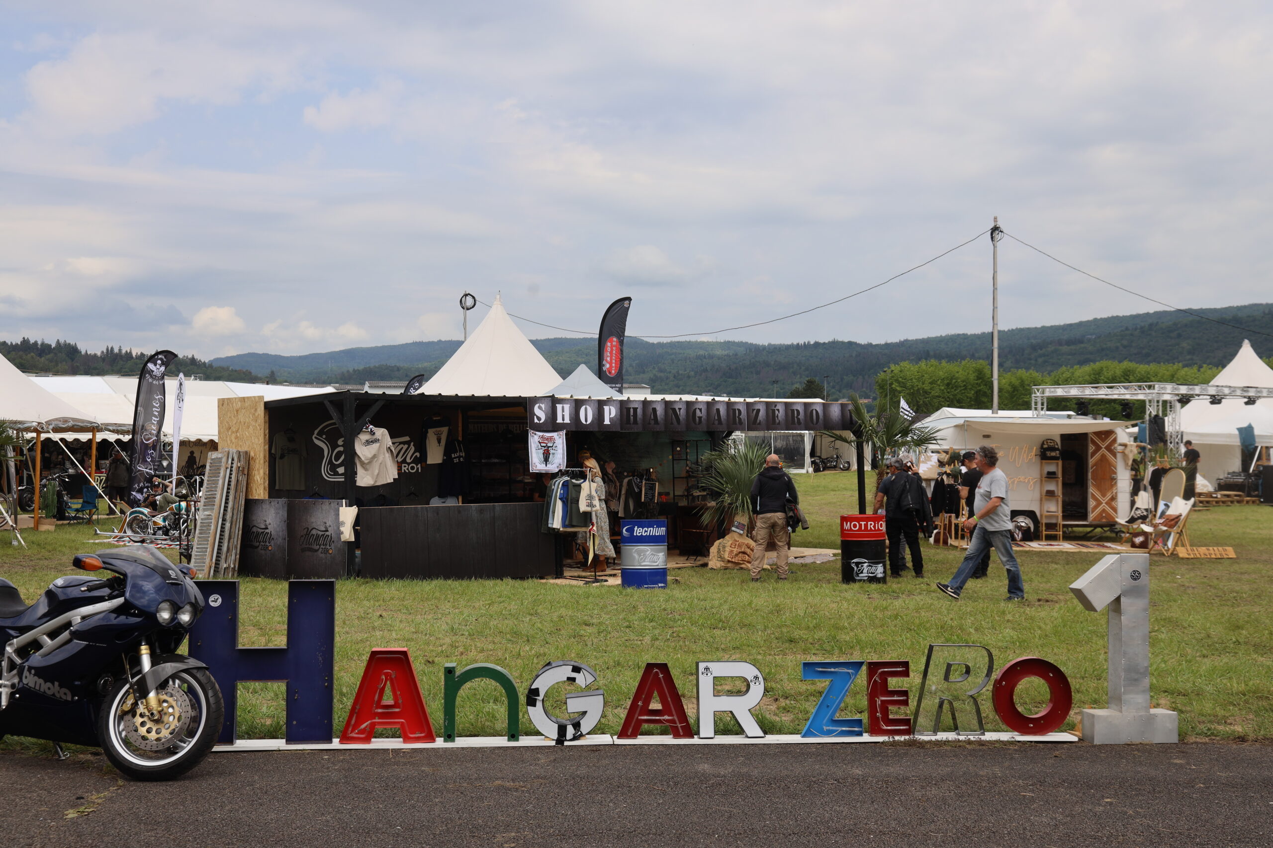 Entrée du festival Hangar Zéro1 Arbent avec un étal et une moto.