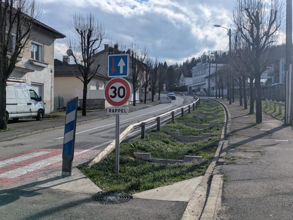 Rue du Colonel Romans Petit à Dortan avec noues paysagères et panneau de limitation de vitesse.