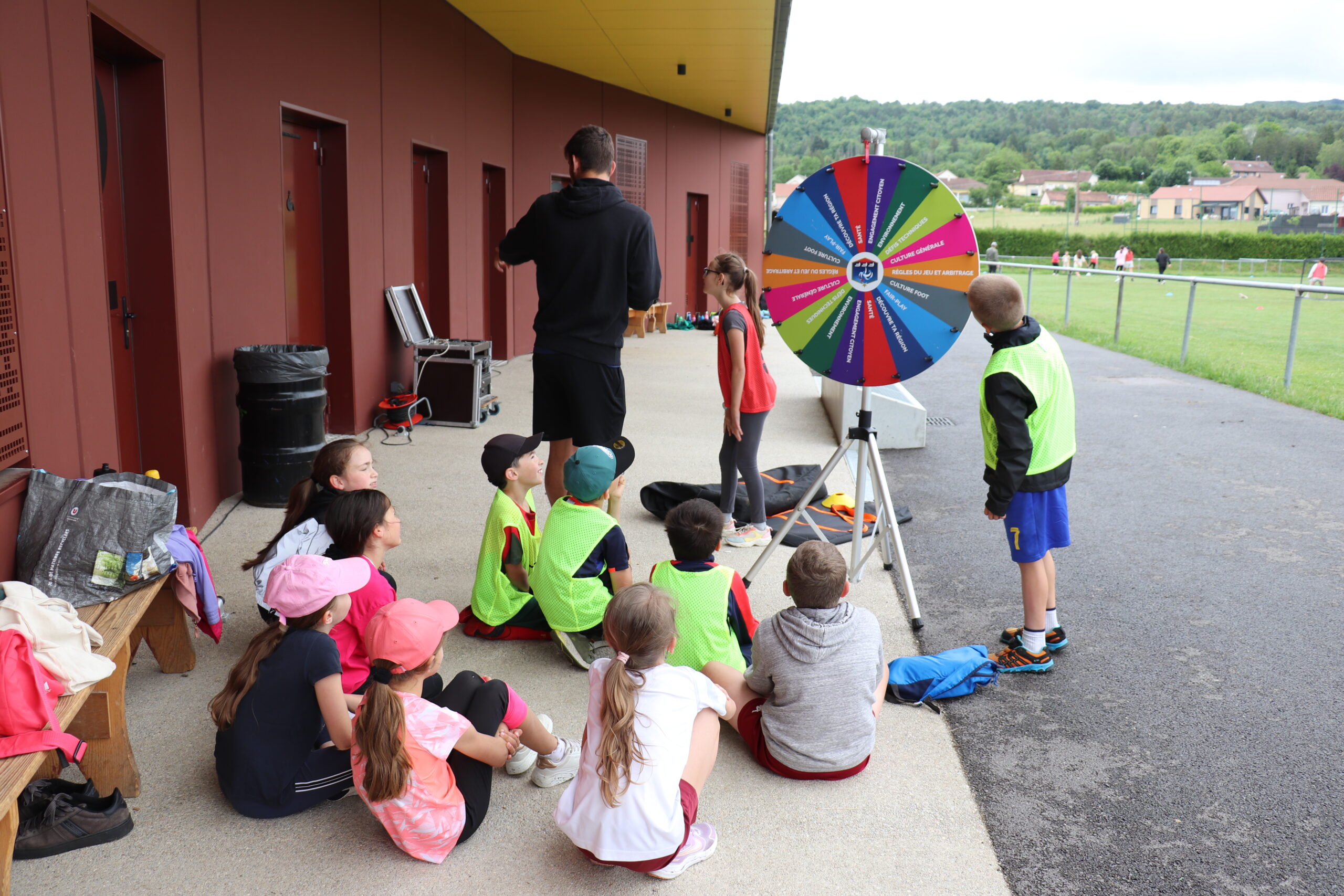 Enfants en cercle jouant à la roue des questions au stade d'Arinthod